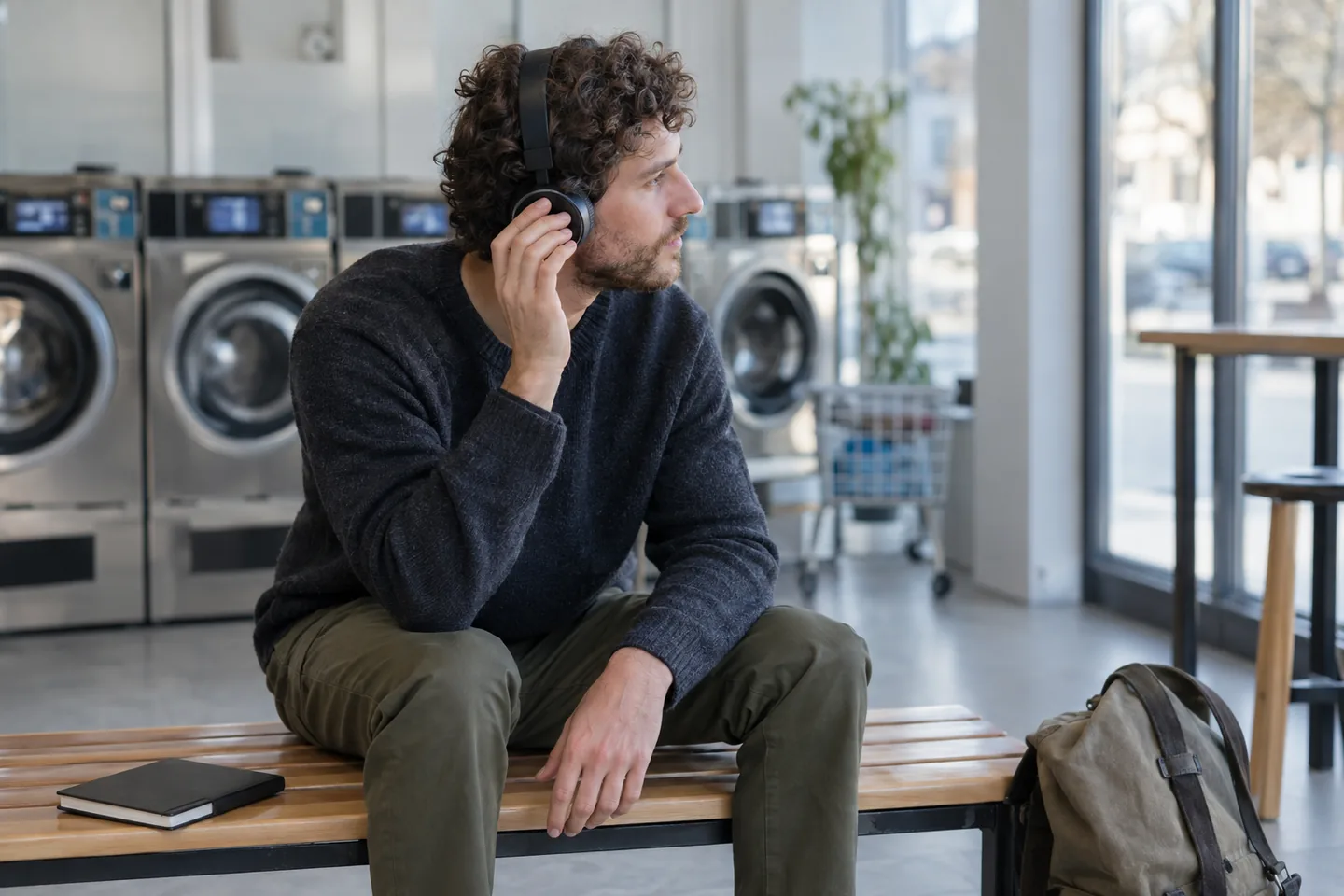 A European man pauses headphone listening on a bench in a bright laundry room