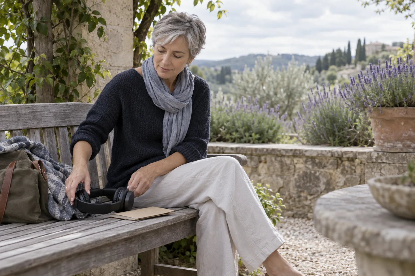 European woman setting headphones beside a paper booklet on a garden bench