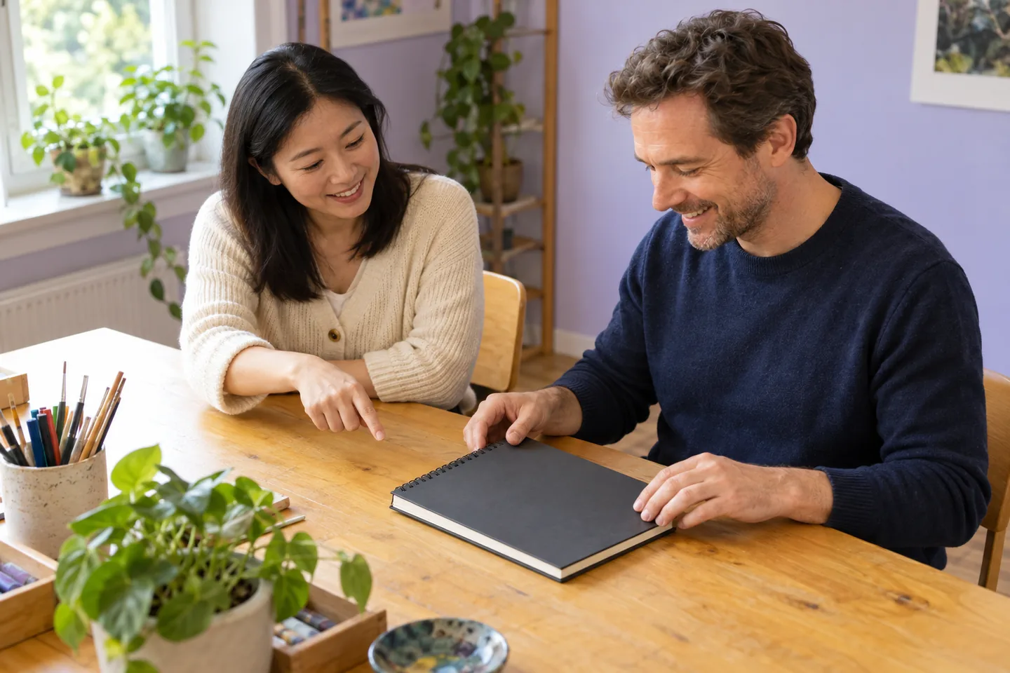 Européen et femme d’Asie orientale pratiquant une demande avec un carnet fermé sur une table d’atelier