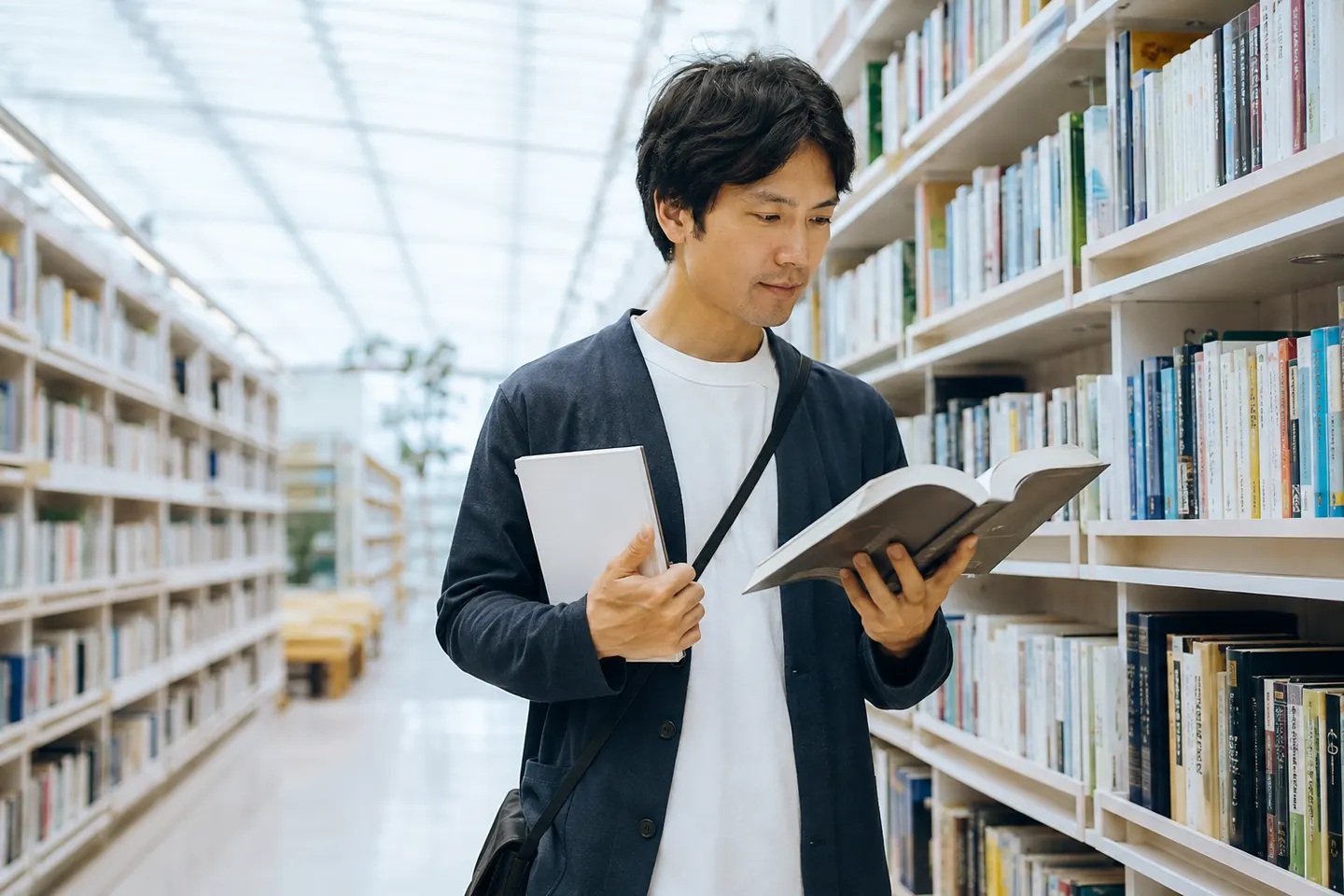 Adult learner in a bright public library comparing a slim beginner workbook with a thicker Japanese reader